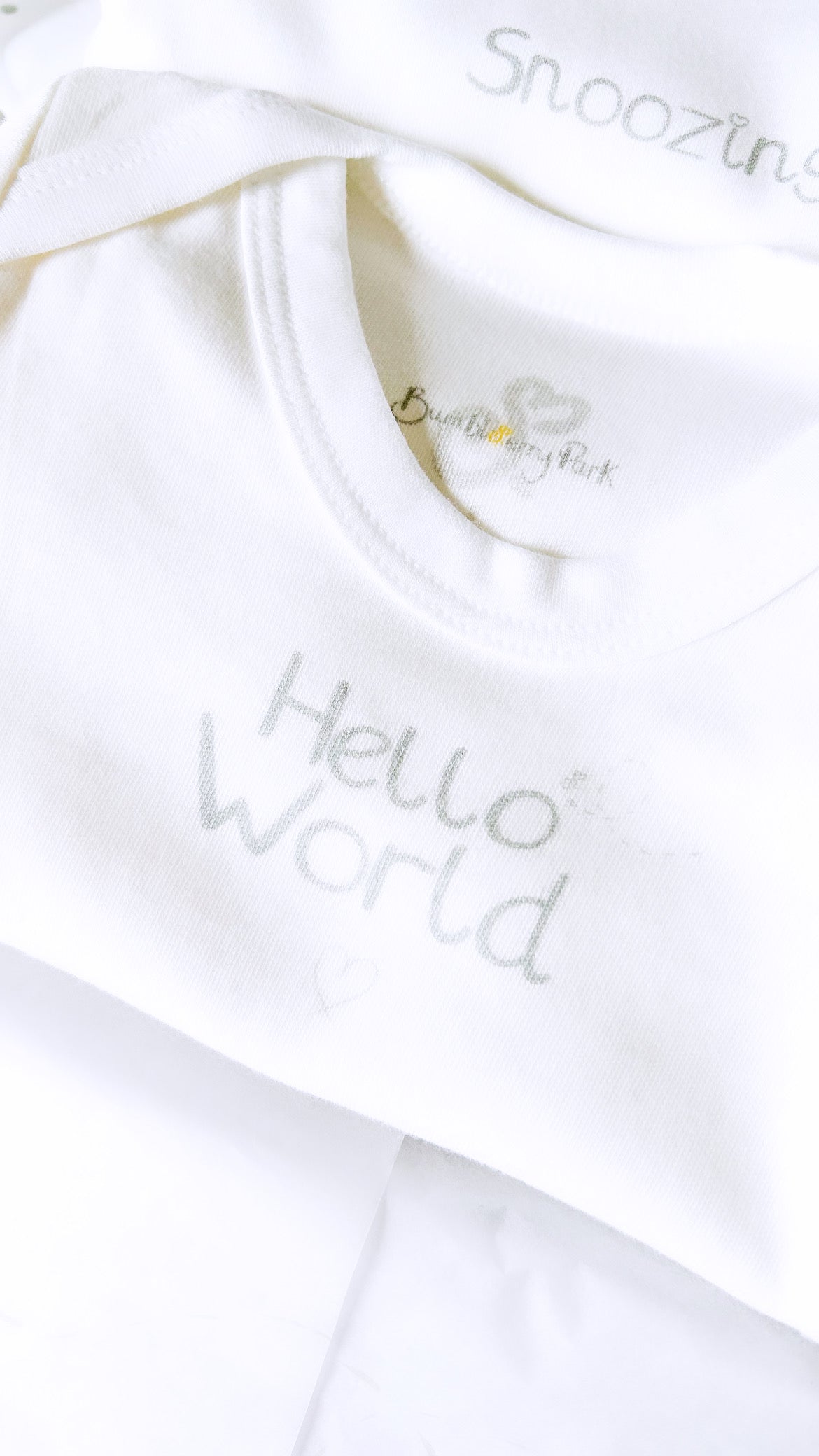 close up of white baby bodysuit with "hello world" print design and bumbleberry park logo