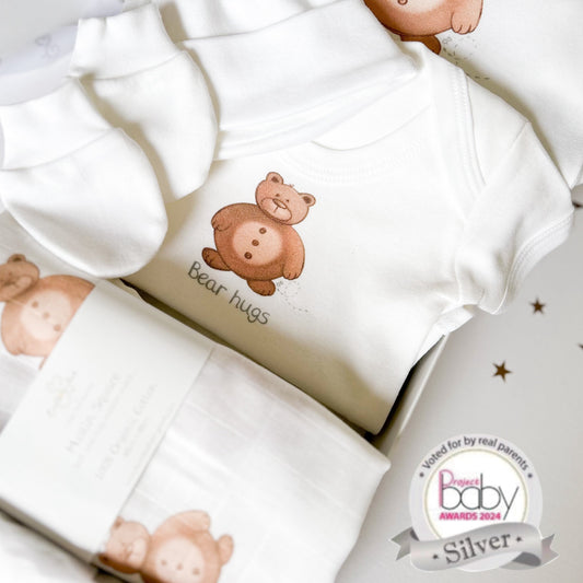 brown teddy bear new baby gift set of a sleepsuit, bodysuit vest, muslin square and hat and mittens with bear hugs slogan, inside a luxury white gift box with satin ribbon gift wrap