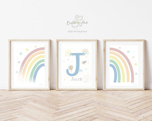 set of three matching rainbow and initial and baby name posters for children's bedroom. Neutral nursery decor prints with personalised initial letter and name print, with travel and transport theme decor with rainbows, sunshine, hot air balloon and aeroplane features