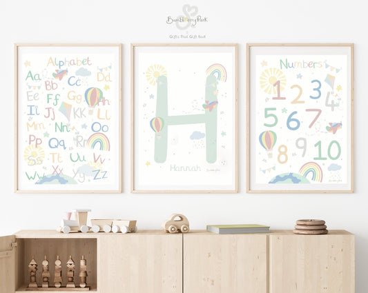 set of three matching alphabet and number posters for children's bedroom. Neutral pastel nursery decor prints with personalised initial letter and name print, with travel and transport theme decor with rainbows, sunshine, hot air balloon and aeroplane designs