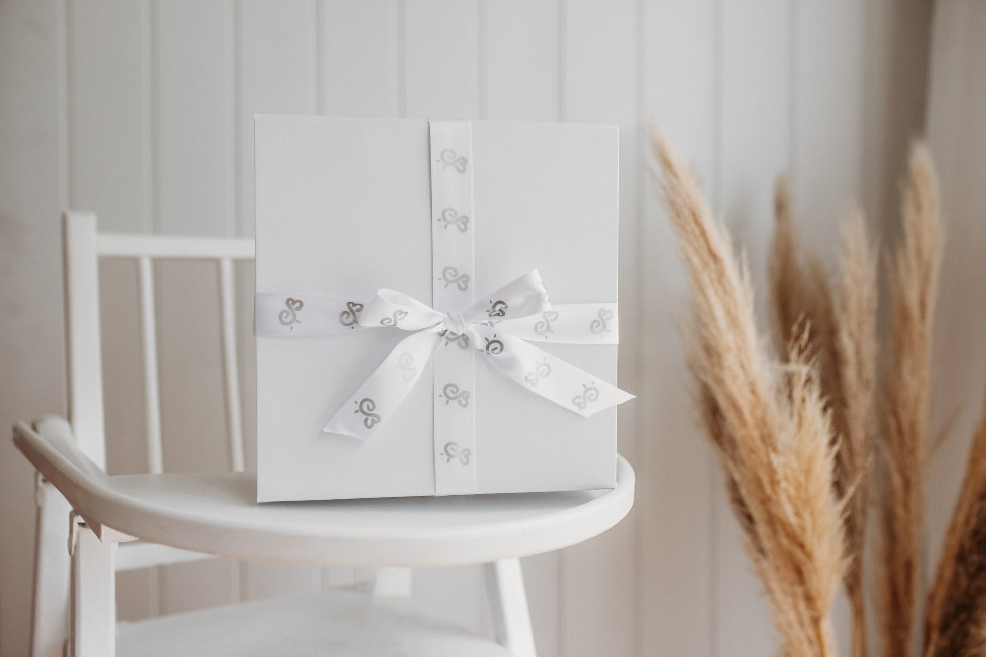 luxury white gloss gift box and wrapping with sati bumbleberry park branded ribbon on a baby's highchair in a nursery