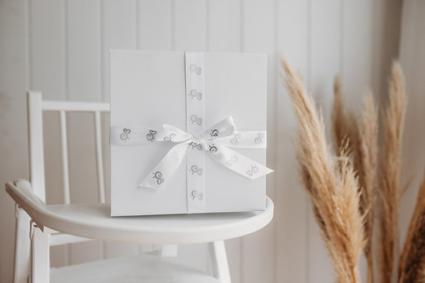 luxury white gift box wrapped in bumbleberry park branded ribbon on a baby's high chair in a child's nursery