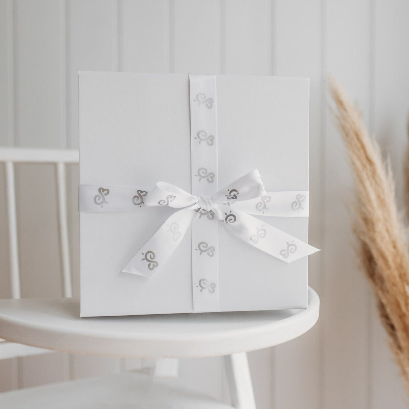 luxury white gloss gift box and wrapping with sati bumbleberry park branded ribbon on a baby's highchair in a nursery