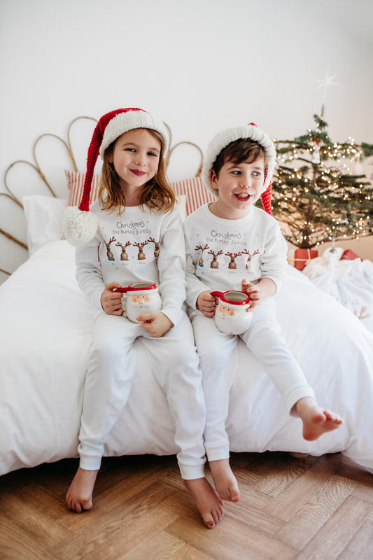 boy and girl sat in santa hats and matching christmas pyjamas with a hot chocolate