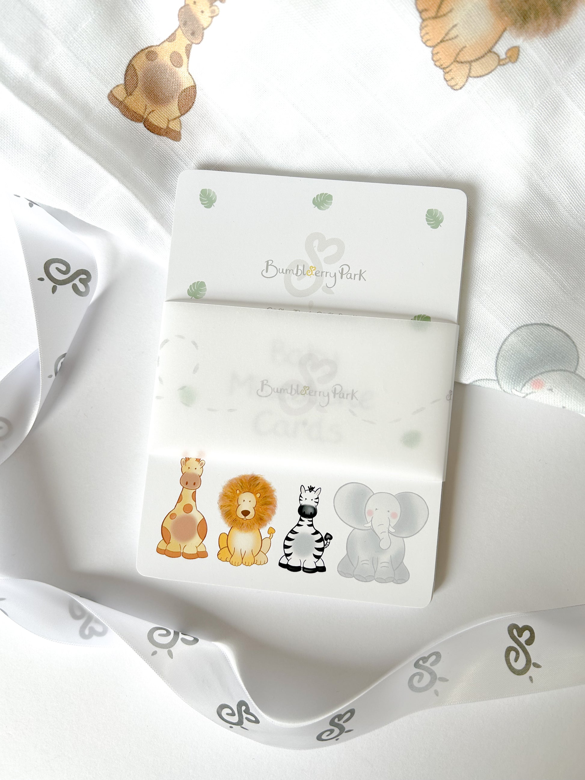 baby milestone card set wrapped in branded ribbon laying on a jungle safari animal muslin swaddle blanket