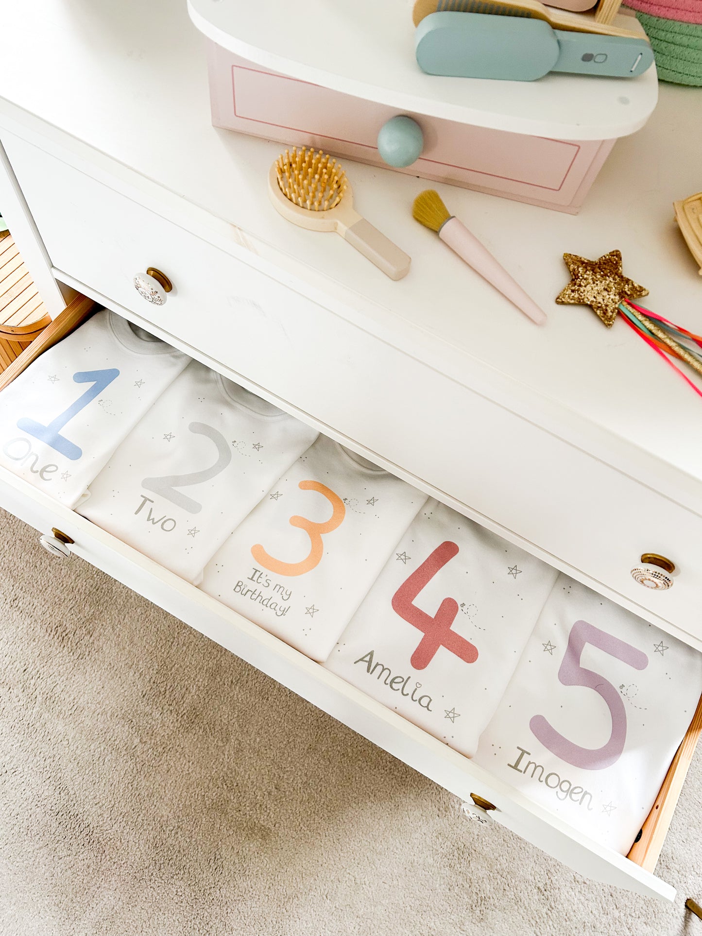 kids bedroom drawers open with five birthday tops inside with ages 1, 2, 3, 4 and 5 in bright rainbow colours and personalised with names and numbers