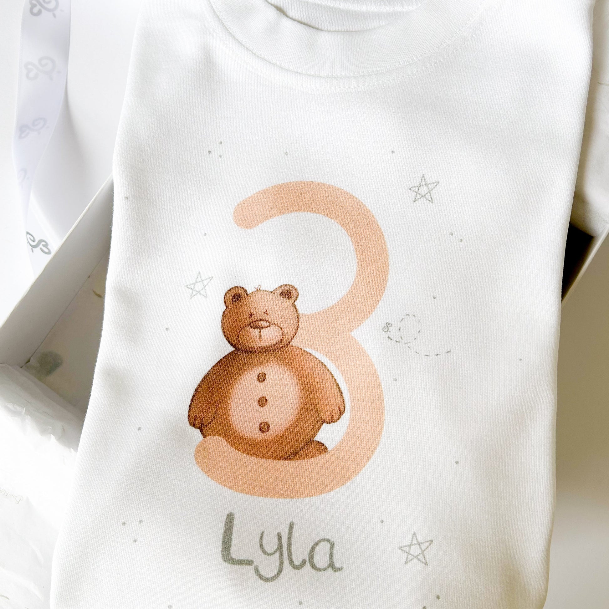 close up on personalised 3rd birthday t-shirt with teddy bear next to a big number 3 in peach fuzz colour and girls name