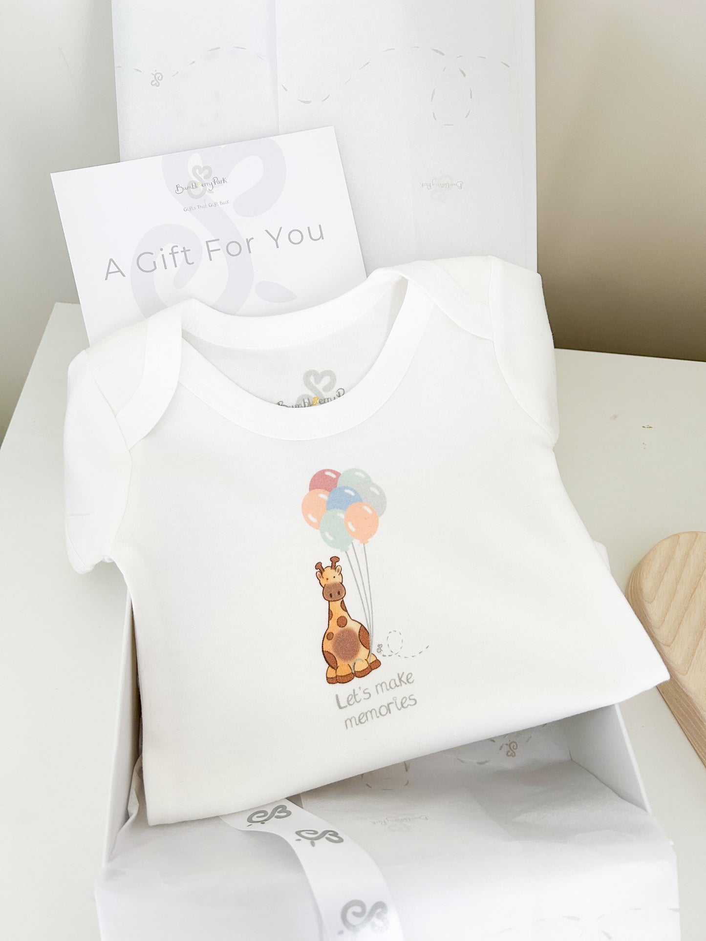 luxury new baby gift set of a babygrow printed with a cute baby giraffe and balloons illustration 