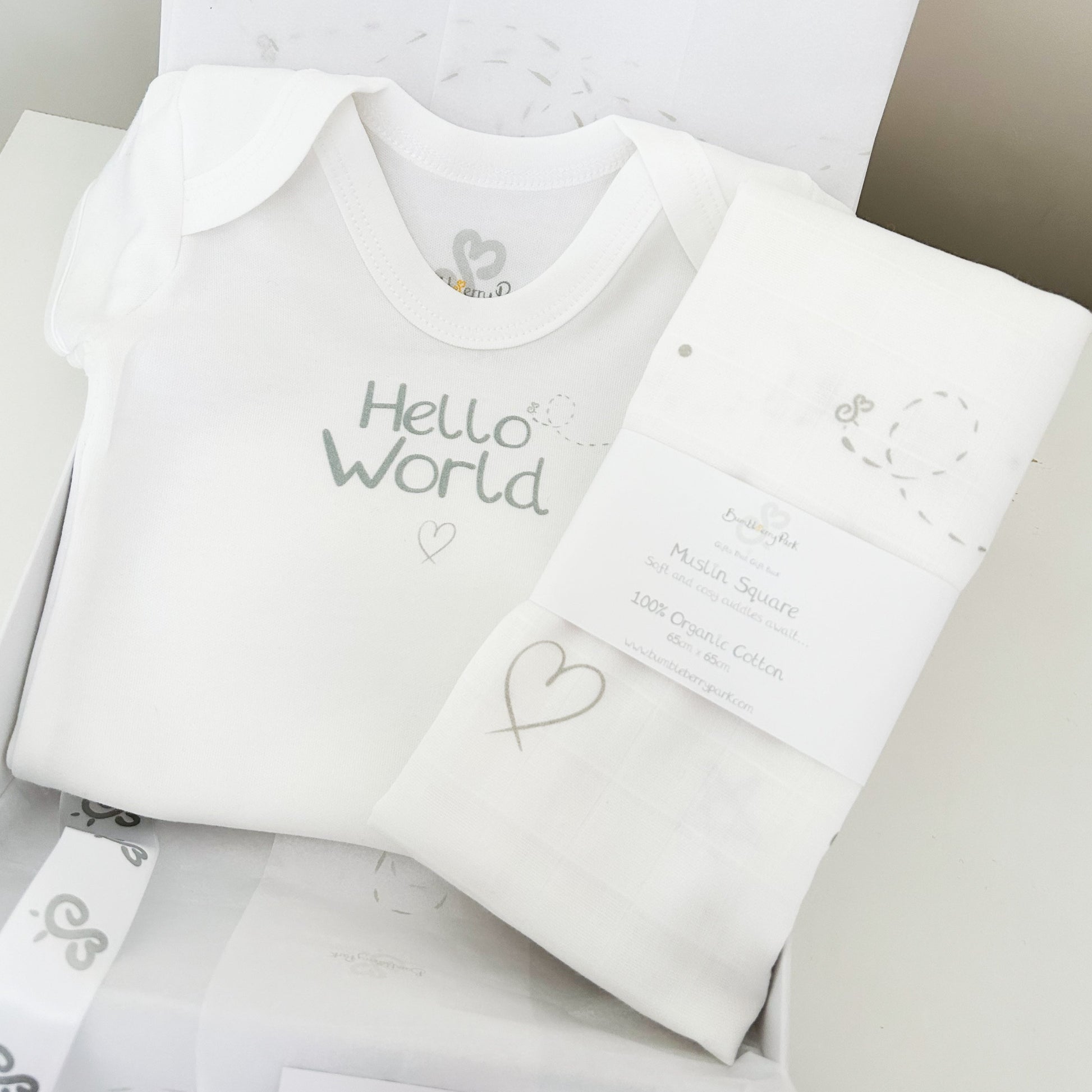white baby bodysuit with "hello world" print design with matching baby muslin swaddle with soft grey neutral hearts, stars, dots and bees pattern