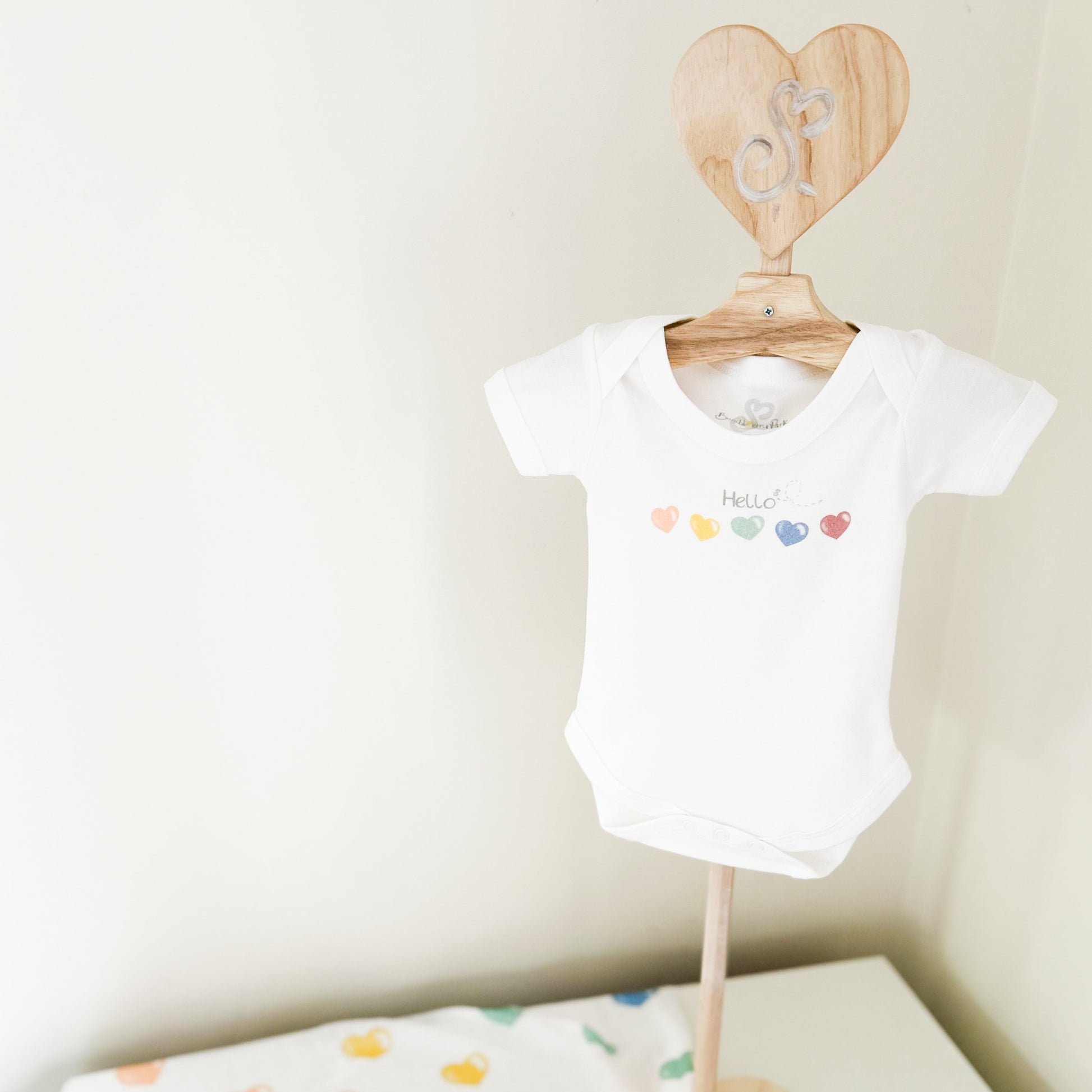 baby clothes stand with a newborn baby vest printed with rainbow coloured love hearts with "hello" quote