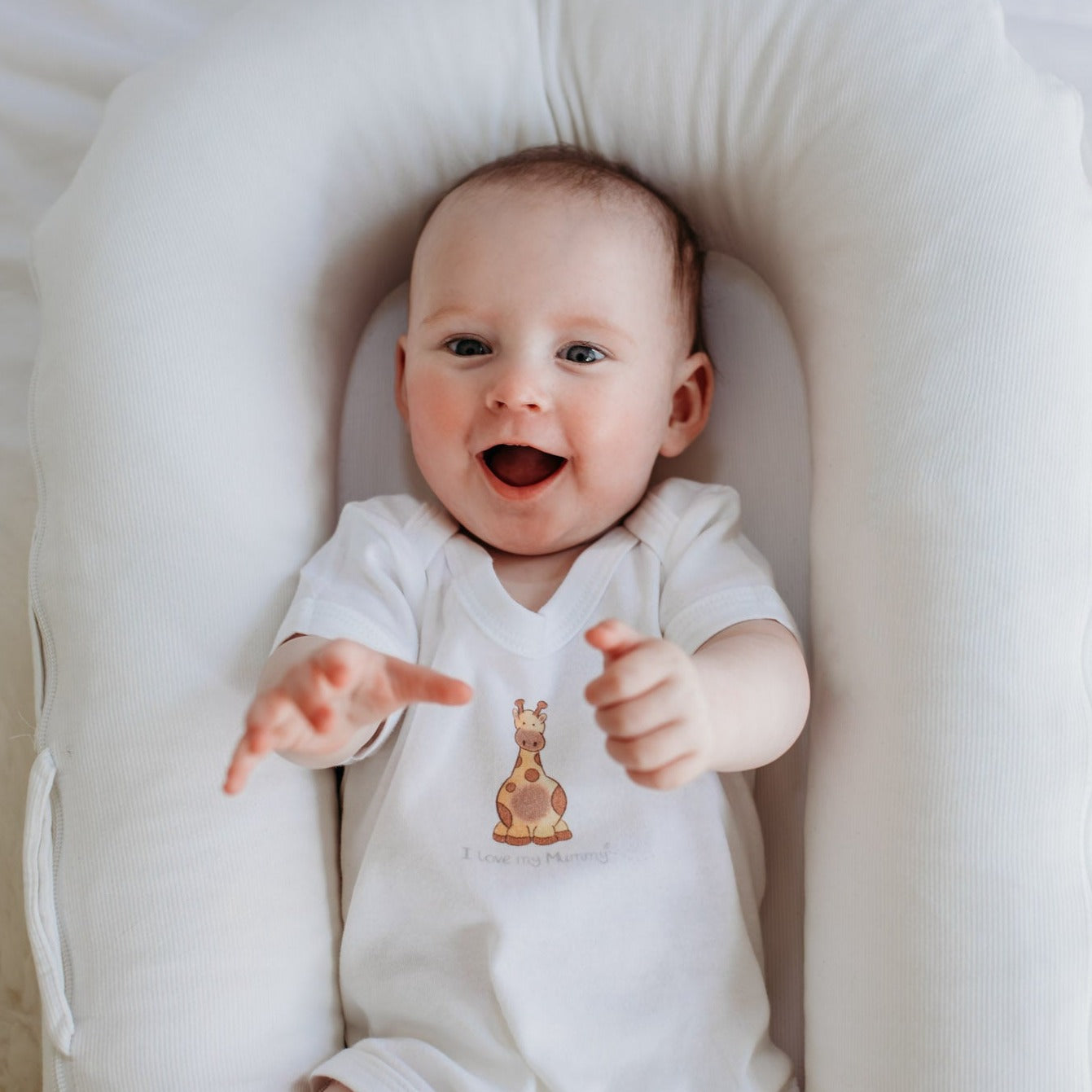 new baby lying in a sleephead giggling wearing a white baby bodysuit with personalised giraffe design