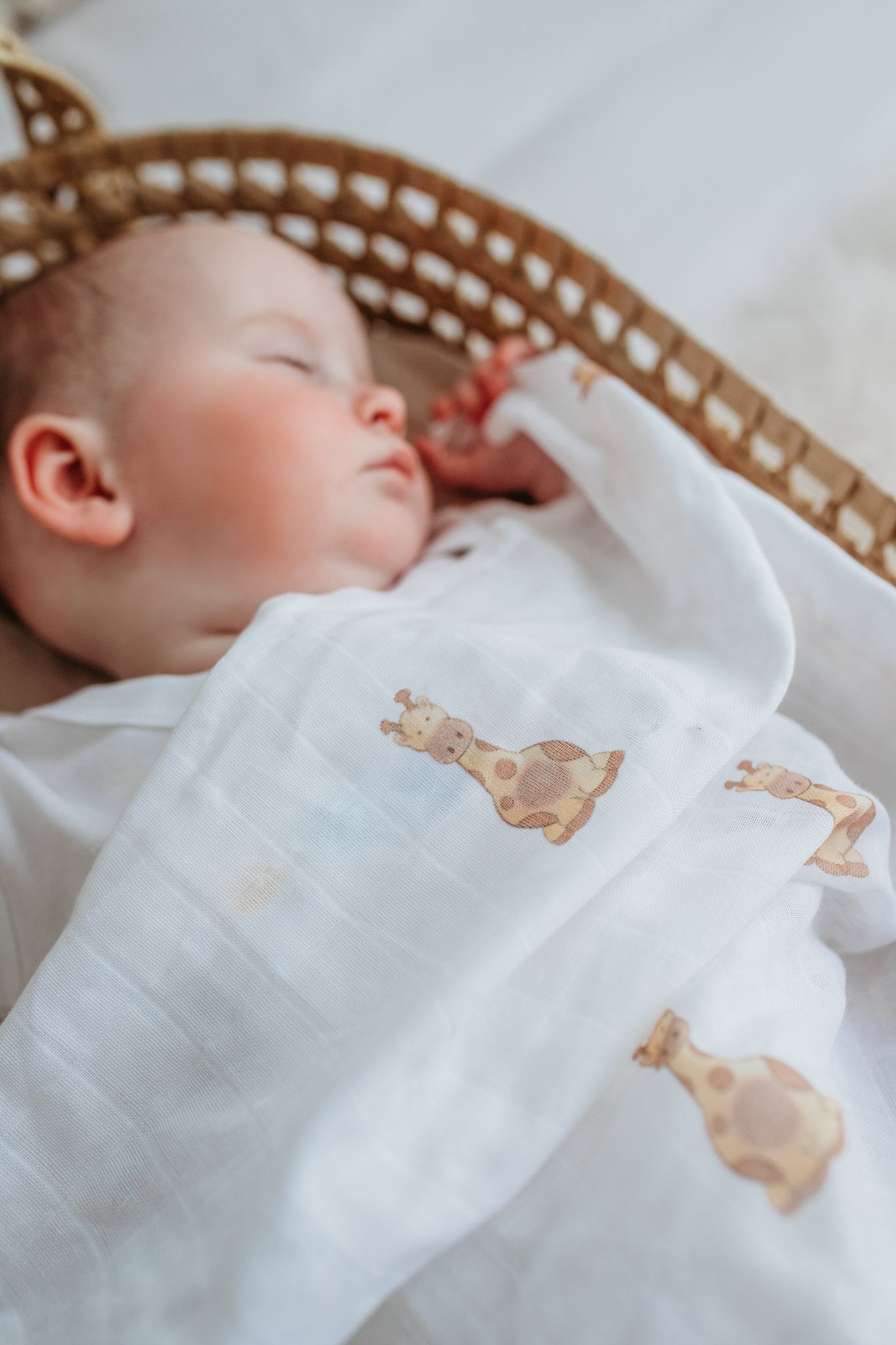 sleeping new baby covered in a soft white organic muslin cloth with a safari giraffe print design