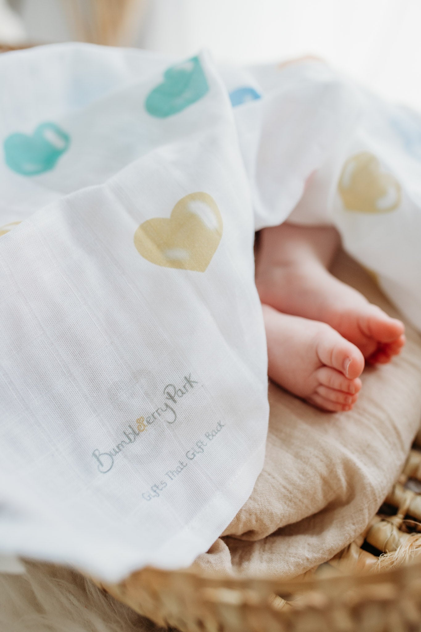 baby toes underneath and soft muslin wrap with bright rainbow coloured love hearts design