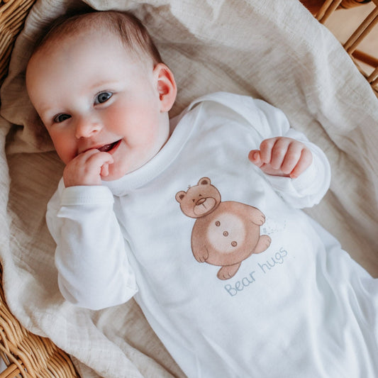 new baby girl wearing a white cotton sleepsuit with a brown teddy bear print with bear hugs text slogan