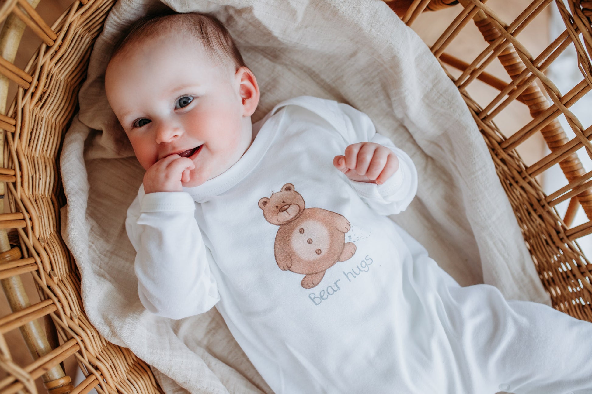 newborn baby laying in a moses basket in soft organic white sleepsuit with woodland bear design and bear hugs motif