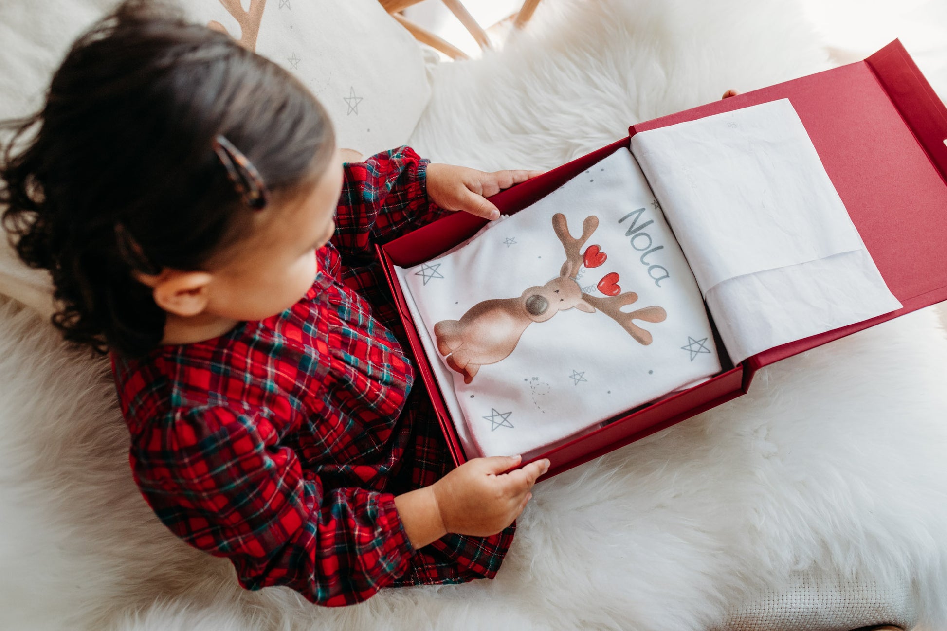 toddler girl opening a christmas box filled with christmas pyjamas with a cute reindeer design on and personalised with her name